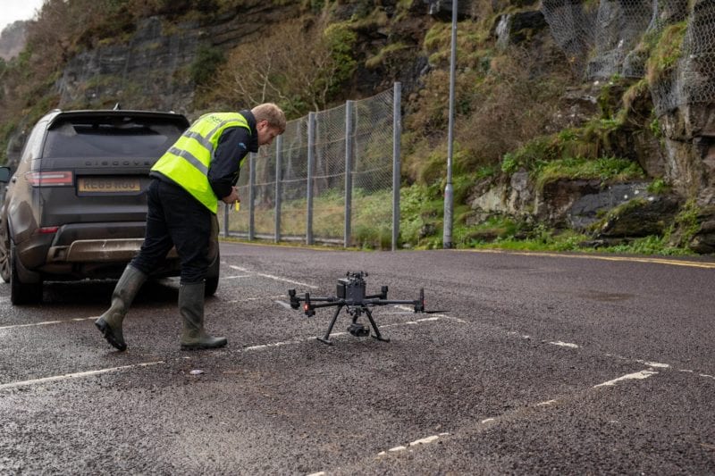 A drone operative inspects a drone before take off in front of a rock face